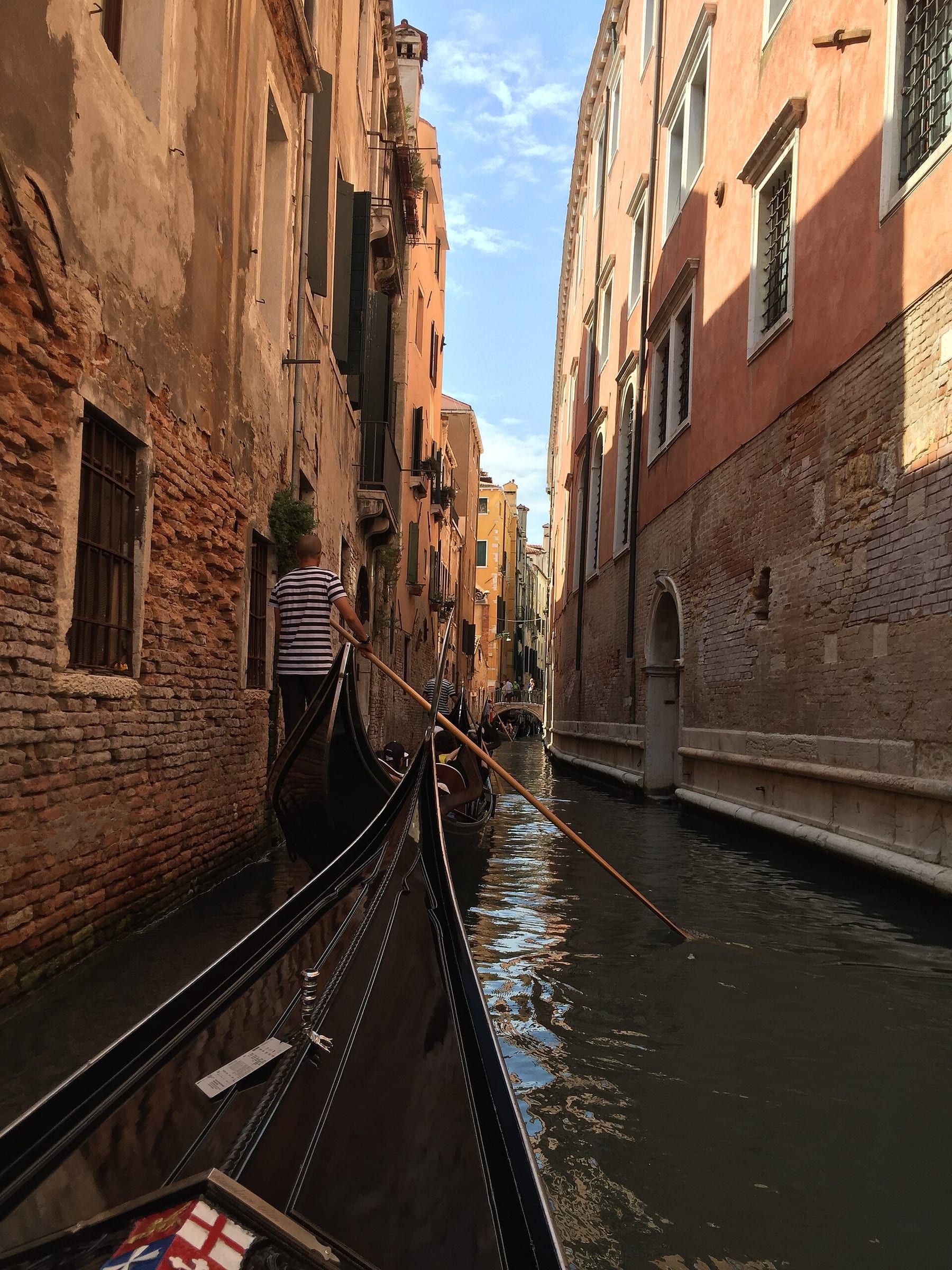 A gondola passing between brick walls in a narrow Venetian side canal, with a low bridge ahead