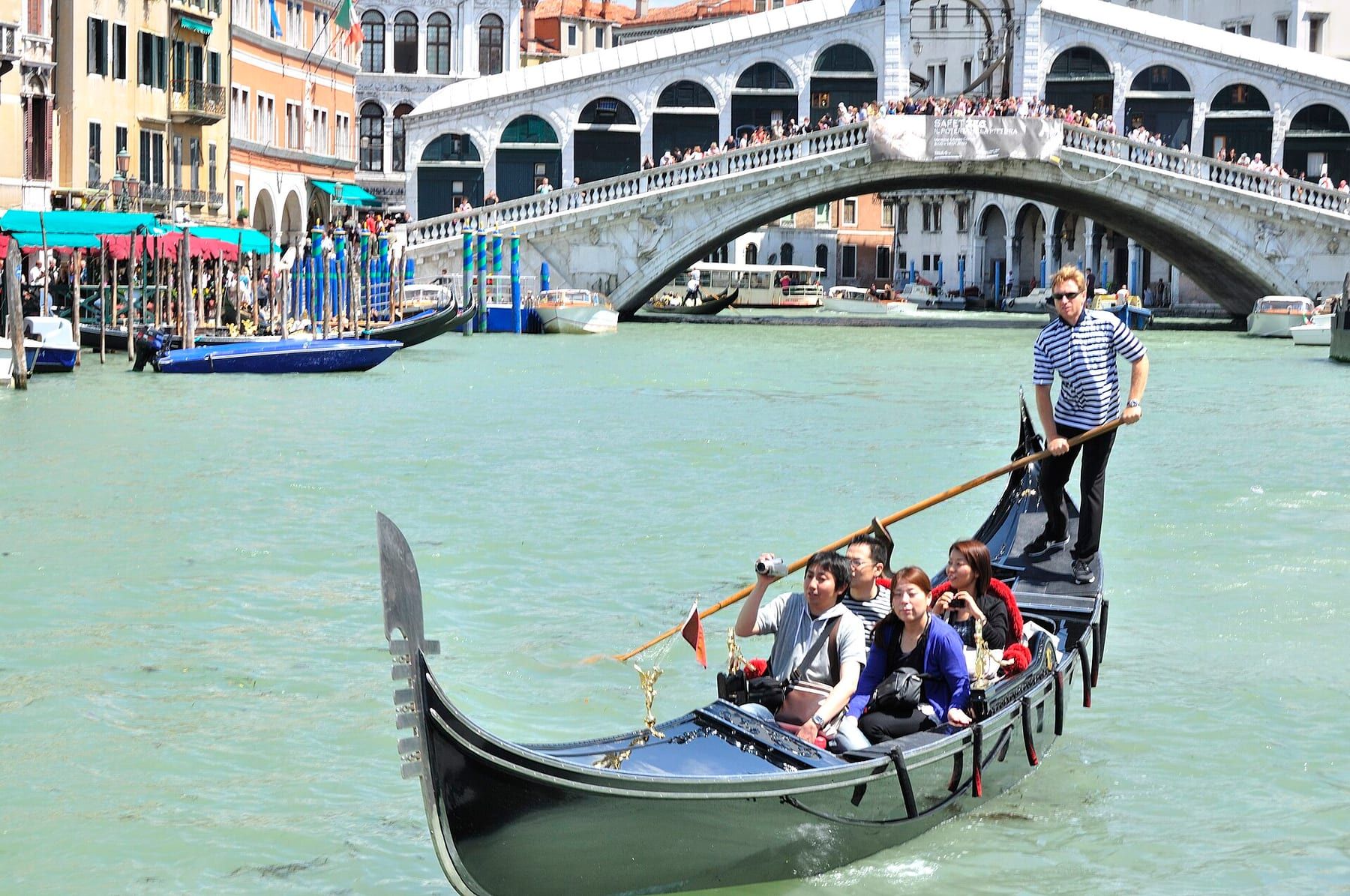 Gondolier in a striped shirt standing at the stern of a gondola, rowing with a single oar