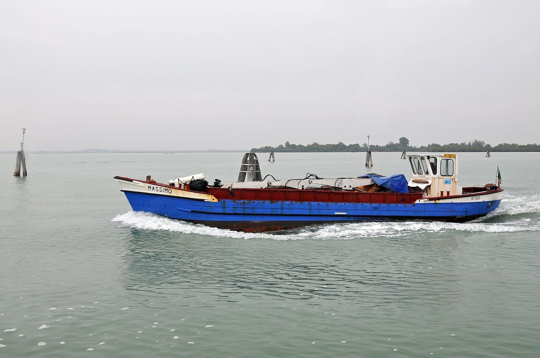 A small passenger boat crossing the Venice lagoon toward the coloured houses of Burano