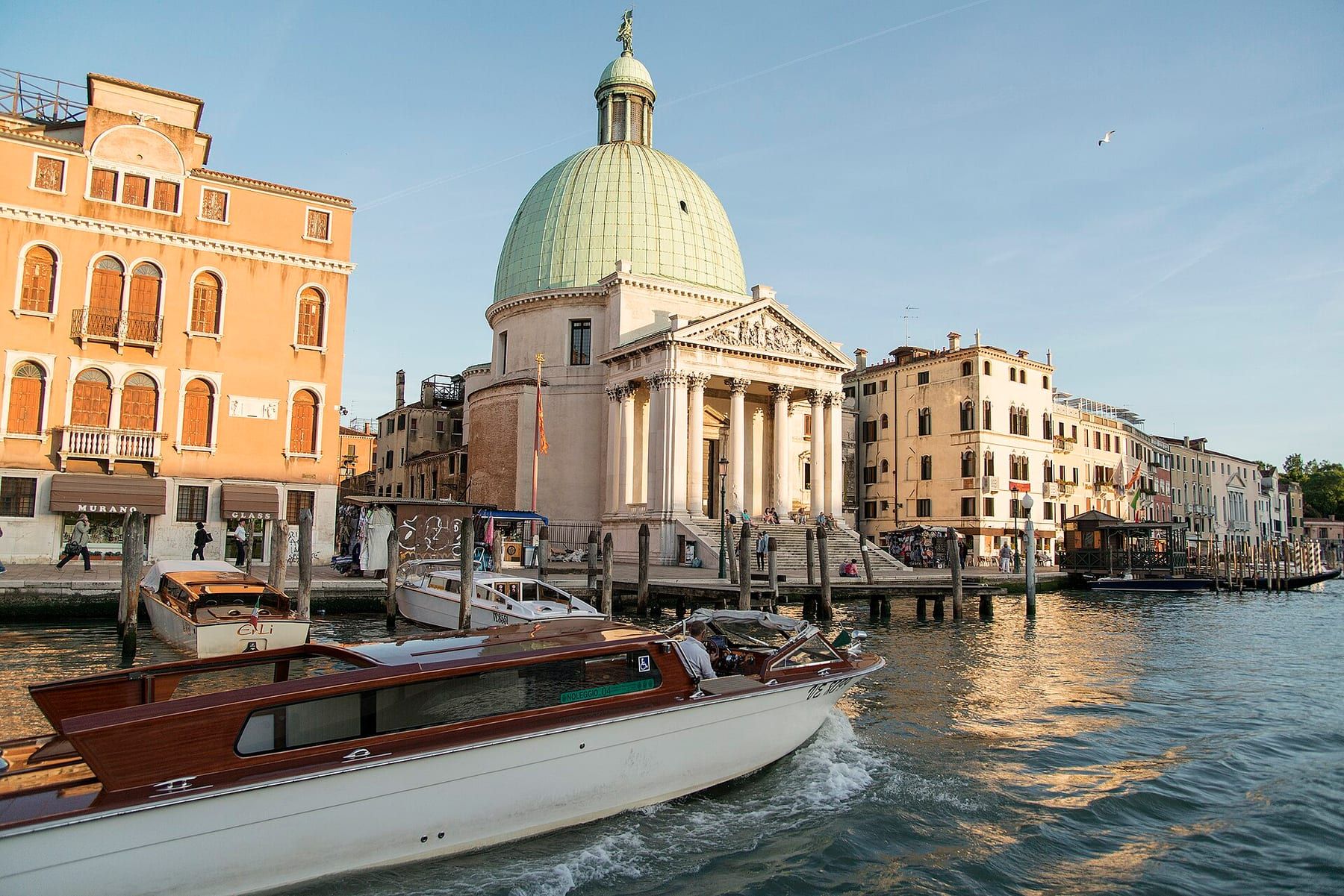 A varnished wooden water taxi moored at a Venice landing stage, its brass fittings catching the light